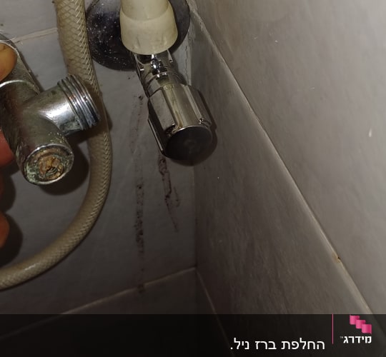 חיבור צינור מים עם ברז מתכת על קיר אריחים